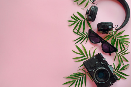 stylish black photo camera with green palm leaves, sunglasses and headphones on trendy pink background, flat lay. modern hipster travel  image. summer vacation, space for textの写真素材