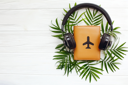 stylish black headphones on passport with plane and green palm leaves on white wooden background. summer vacation concept, creative flat lay. modern travel photo. space for textの写真素材