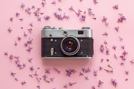 stylish old photo camera on pink background with lilac flowers. creative travel trendy flat lay with space for text. modern fashion and hipster image. summer vacation conceptの写真素材