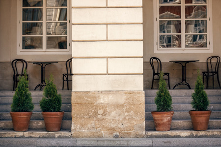 beautiful old building wall, table with wooden chairs and trees, modern exterior of cafe in european...