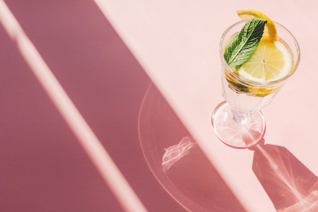 summer vacation and party concept. fresh cocktail with lemon and mint in vintage glass on trendy pink paper background in sun light. mojito. refreshing drinks. space for textの写真素材
