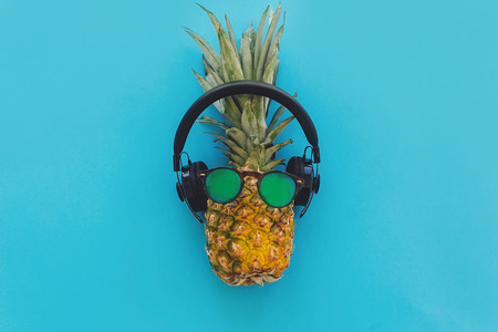 pineapple in stylish hipster sunglasses and black headphones on blue trendy paper background, flat...