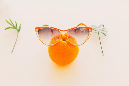 orange in stylish sunglases with palm leaf on pastel yellow paper trendy background. modern summer image, with space for text. vacation concept. funny and juicy abstractの写真素材
