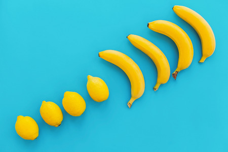 summer flat lay. yellow bananas with lemons in line on blue paper trendy background, flat lay. bright colorful photo, with space for text. juicy abstract background, pop art styleの写真素材