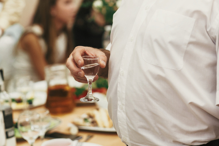 man holding glass of vodka and toasting at wedding reception. people cheering and making toasts with glasses of drinks at feast  in restaurantの写真素材