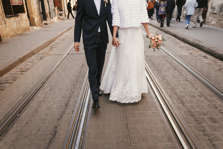 gorgeous bride with bouquet and groom holding hands and walking down the road in city street in Europe.の写真素材