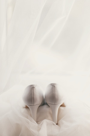 beautiful stylish shoes on luxury silk wedding dress. simple white shoes on white gown with lace floral ornaments, bridal morning preparationsの写真素材