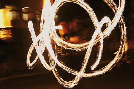 amazing fire show at night at festival or wedding party. Fire dancers swing, spinning fire and man juggling with bright sparks in the night. fire show performance and entertainmentの写真素材
