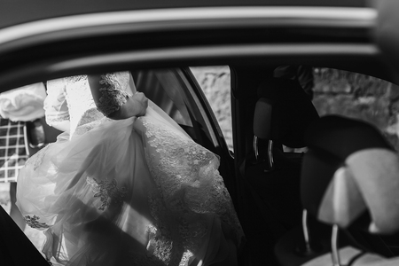 moment of bride in luxury wedding dress getting in car. bride in lace gown sitting in stylish car. black and white photoの写真素材