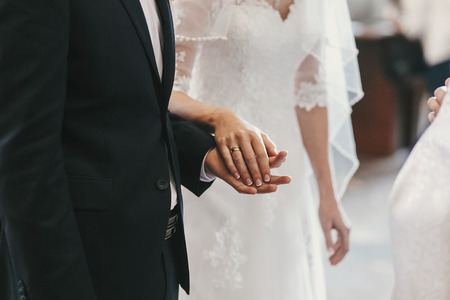 beautiful bride and groom hands exchanging wedding rings in church during wedding ceremony. spiritual holy matrimony. wedding couple and priest putting on ringsの写真素材