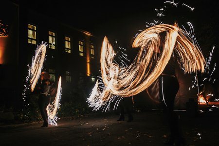 Fire dancers swing, spinning fire and man juggling with bright sparks in the night. fire show performance and entertainment. amazing fire show at night at festival or wedding party.の写真素材