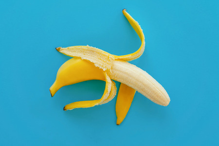 opened banana on bright blue paper, trendy background. fruit modern flat lay. juicy summer vitamin...