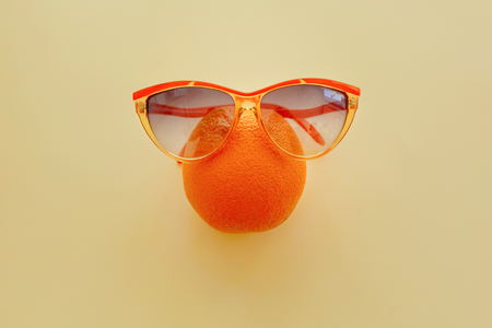 orange in sunglasses on pastel yellow paper, trendy flat lay. summer vacation idea. juicy fruit eat and diet concept. pop art style. creative minimalism . space for textの写真素材