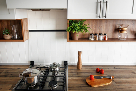 wooden board with knife, tomatoes on modern kitchen countertop and shelves with spices in glass jars. cooking food. Stylish gray kitchen interior design in scandinavian style with steel stoveの写真素材