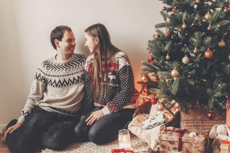 stylish couple in sweaters hugging and smiling at christmas tree in cozy evening room. atmospheric moments. merry christmas and happy new year concept. happy holidaysの写真素材