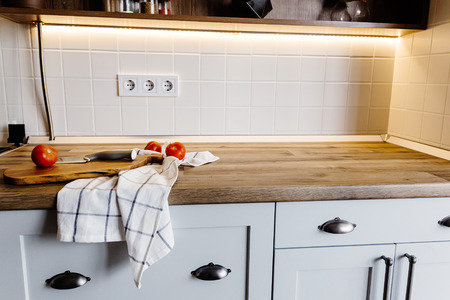 wooden board with knife, tomatoes, towel on modern kitchen countertop and shelf with spices and plants. cooking food. Stylish kitchen interior design in scandinavian styleの写真素材