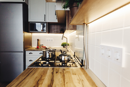 Cooking on Modern Kitchen  in scandinavian style. stylish kitchen interior with modern furniture and stainless steel appliances. wooden countertop, steel stove, board,knife and spices, tomatoesの写真素材
