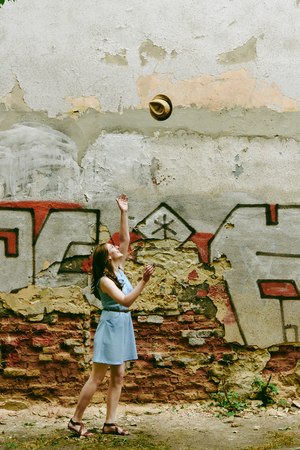 stylish woman hipster throwing her hat at old wall in european streets in sunny morning, space for textの写真素材