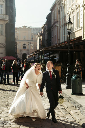 happy bride and stylish groom running with funny emotions on the background old sunny cityの写真素材