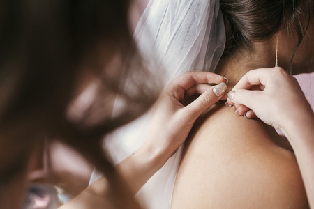 bridesmaids and mother helping gorgeous bride getting ready for wedding. beautiful woman hands...