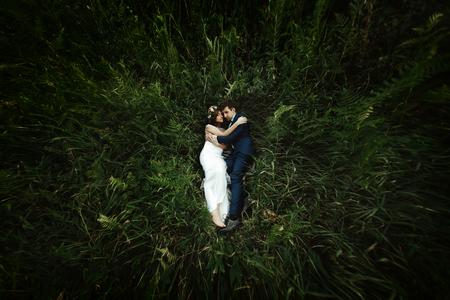 luxury happy bride and stylish groom lying on grass under sunny rocks in amazing mountains, tender momentの写真素材