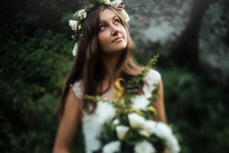 stylish sensual boho bride with bouquet on background of rocks and woods