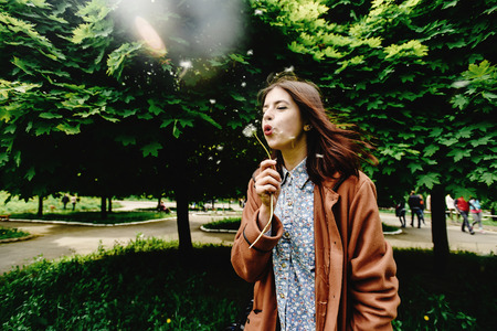 stylish beautiful hipster girl holding dandelion and having fun in city park in sunny spring timeの写真素材