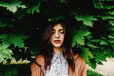 beautiful brunette woman standing under amazing green tree crown in city park in sunny springtime, ecology conceptの写真素材