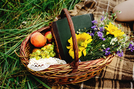 beautiful picnic wicker basket with colorful bouquet fruits and books on tweed plaid, happy bride and stylish groom legsの写真素材