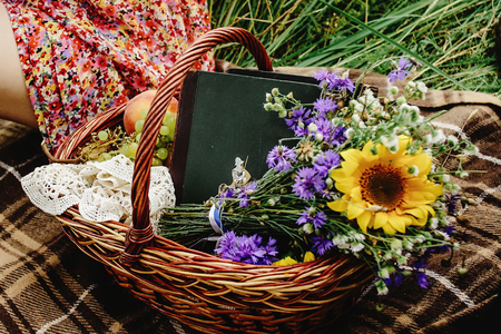beautiful picnic wicker basket with colorful bouquet fruits and books on tweed plaid, happy bride and stylish groom legsの写真素材