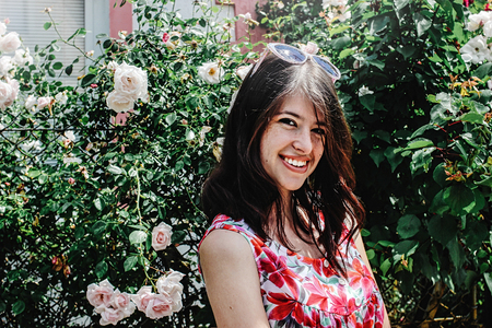 stylish brunette beautiful woman smiling in floral dress in sunny street on background of rosesの写真素材