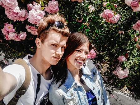 stylish couple hipsters traveling in europe city and having selfie on background of sunny rosesの写真素材