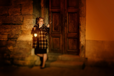 Mysterious beautiful woman in vintage 30's dress and coat holding lantern and cigarette on holder, night in paris conceptの写真素材