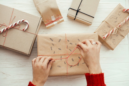 woman in red sweater wrapping stylish christmas gift with red robe. modern craft presents on white...