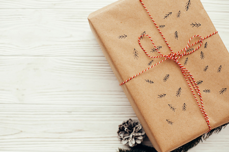 christmas flat lay. stylish present with red ribbon and tree pattern. copy space. modern craft gift on white wooden background. seasonal greetings card mock-up. merry christmasの写真素材