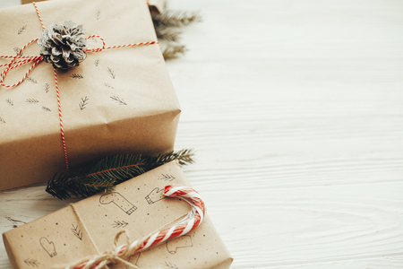 christmas stylish presents with red ribbon, candy cane, pine branches, cones. copy space. modern craft gifts on white wooden background. seasonal greetings card mock-up.の写真素材