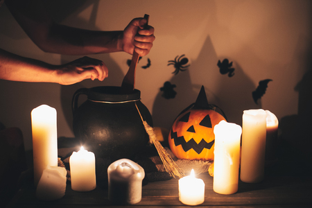 witch hand boiling potion for spell, with jack o lantern pumpkin with candles, broom and bats, ghosts on background in dark spooky room. Happy Halloween. spooky atmospheric momentの写真素材