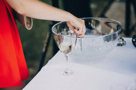 woman getting ice for stylish champagne drink on wedding table. luxury drinks for celebration, reception outdoors. catering. christmas feastの写真素材