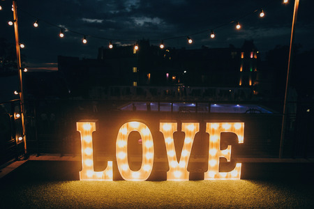 big white love letters in light bulbs for photo booth at wedding reception in night outdoors. love word lights, stylish evening decor for wedding ceremonyの写真素材