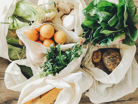 fresh vegetables in eco cotton bags on table in the kitchen. lettuce, corn, potatoes, apricots, bananas, rucola, mushrooms from market. zero waste shopping concept.   ban plasticの写真素材