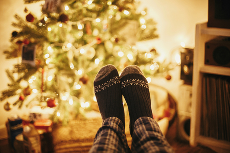 festive socks on old wooden chair on background of golden beautiful christmas tree with lights in festive room. relax time. cozy winter holidays. warm atmospheric moment.の写真素材