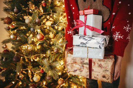 hands holding many Christmas gift boxes at golden beautiful christmas tree with lights in festive room. winter holiday atmospheric moments. seasons greetings. Merry Christmasの写真素材