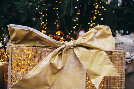 Golden gift boxes under christmas tree in european city center. Big presents with bows on background of christmas lights. Festive decor of city streets in winter holidaysの写真素材