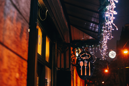 Stylish christmas decorations, garland lights on window of cafe or restaurant, food sign, in european city street. Festive decor and illumination in city center, winter holidaysの写真素材