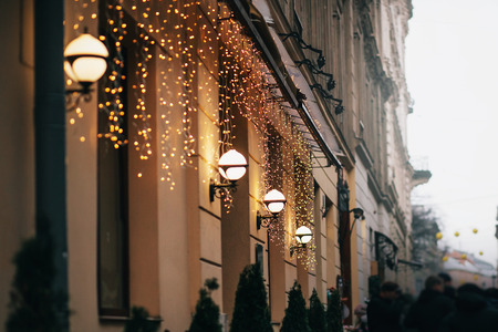Stylish christmas decorations, garland lights and lamps on old building and crowd of people in european city street. Festive decor and illumination in city center, winter holidaysの写真素材