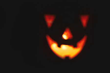 Halloween pumpkin with scary glowing face on black background isolated. Jack-o'-lantern glowing pumpkin in dark. Trick or treat. Space for text. Backdrop for halloween. Blurred imageの写真素材
