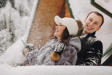 Stylish couple playing with snow in wooden cabin on background of winter snowy  mountains. Happy...