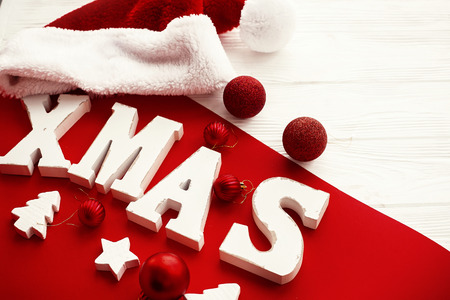 Merry Christmas. Xmas wooden word with red and gold baubles and santa hat on rustic bright background. Seasons greeting card, Stylish traditional holiday image. Christmas textの写真素材