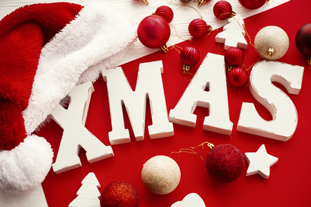 Xmas wooden word with red and gold baubles and santa hat on rustic bright background. Merry Christmas. Seasons greeting card, Stylish traditional holiday imageの写真素材