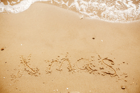Xmas text written on sandy beach with wave near sea. Travel and vacations. Space for text. Merry Christmas concept, happy holidays.の写真素材